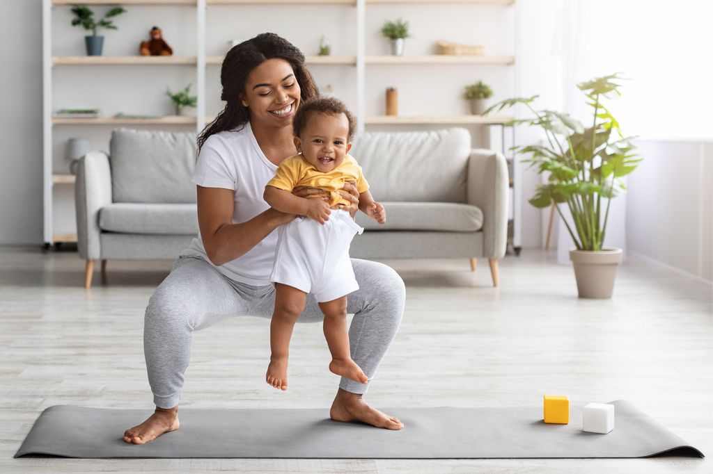 Mother doing a squat with her baby in her arms at home 