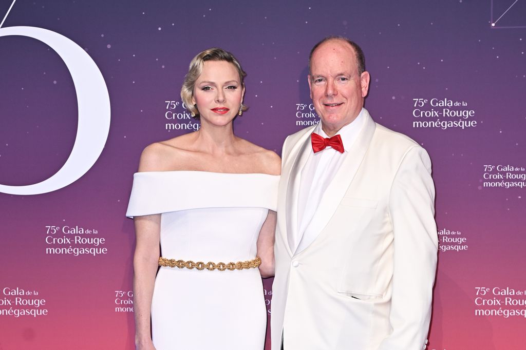 Princess Charlene in a white dress with Prince Albert in a white tuxedo with red bowtie