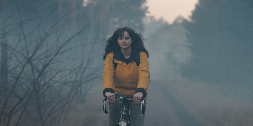 Still image from Dark featuring a girl riding a bike down a foggy path in a yellow jacket