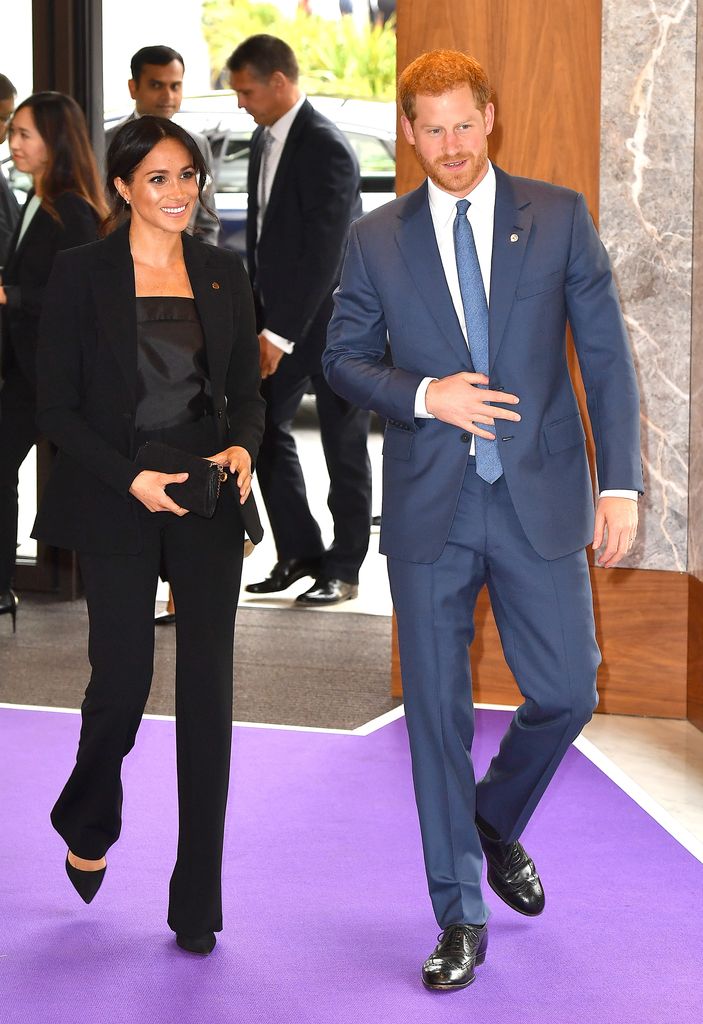 Prince Harry in a blue suit and Meghan Markle in black trousers