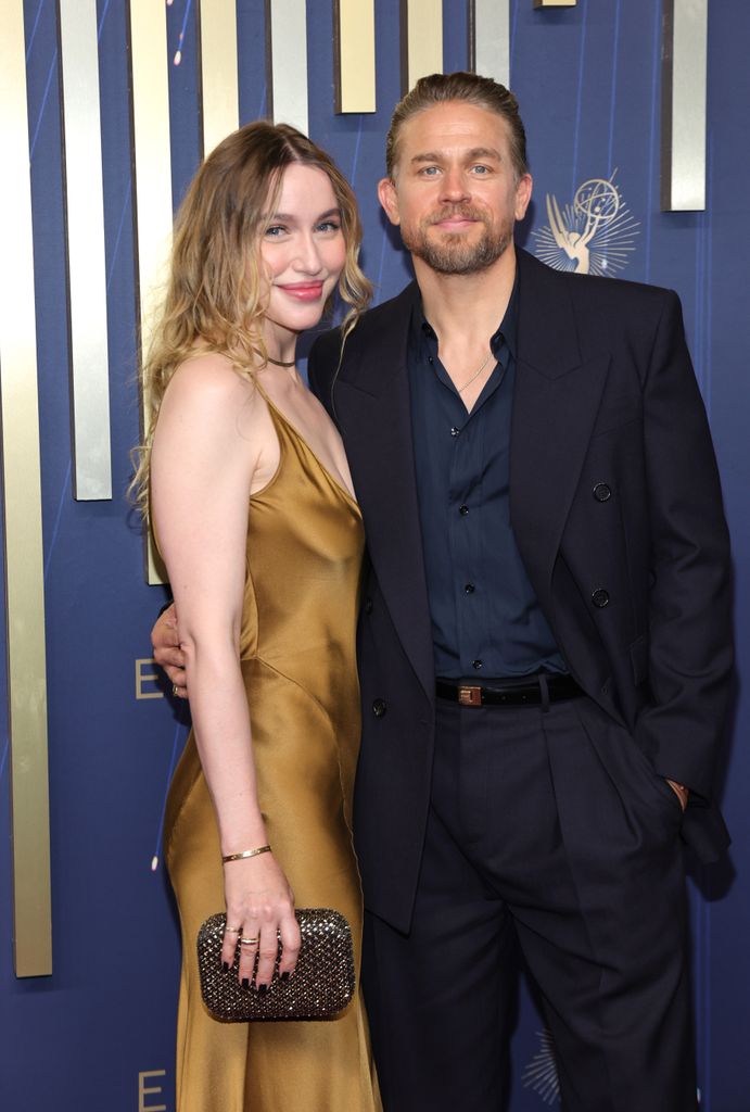Morgana McNelis in gold dress and Charlie Hunnam in navy suit at the 77th Primetime Emmy Awards at Peacock Theater 