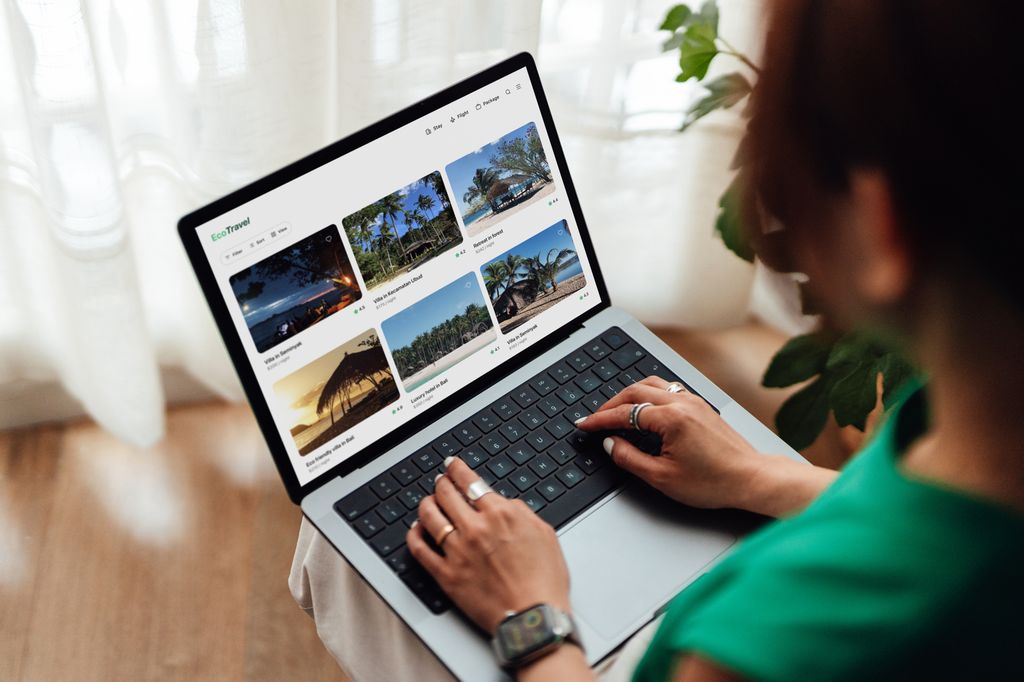 Young woman using laptop showing online travel booking platform with various sustainable hotels. Concept of green travel and sustainable holiday.