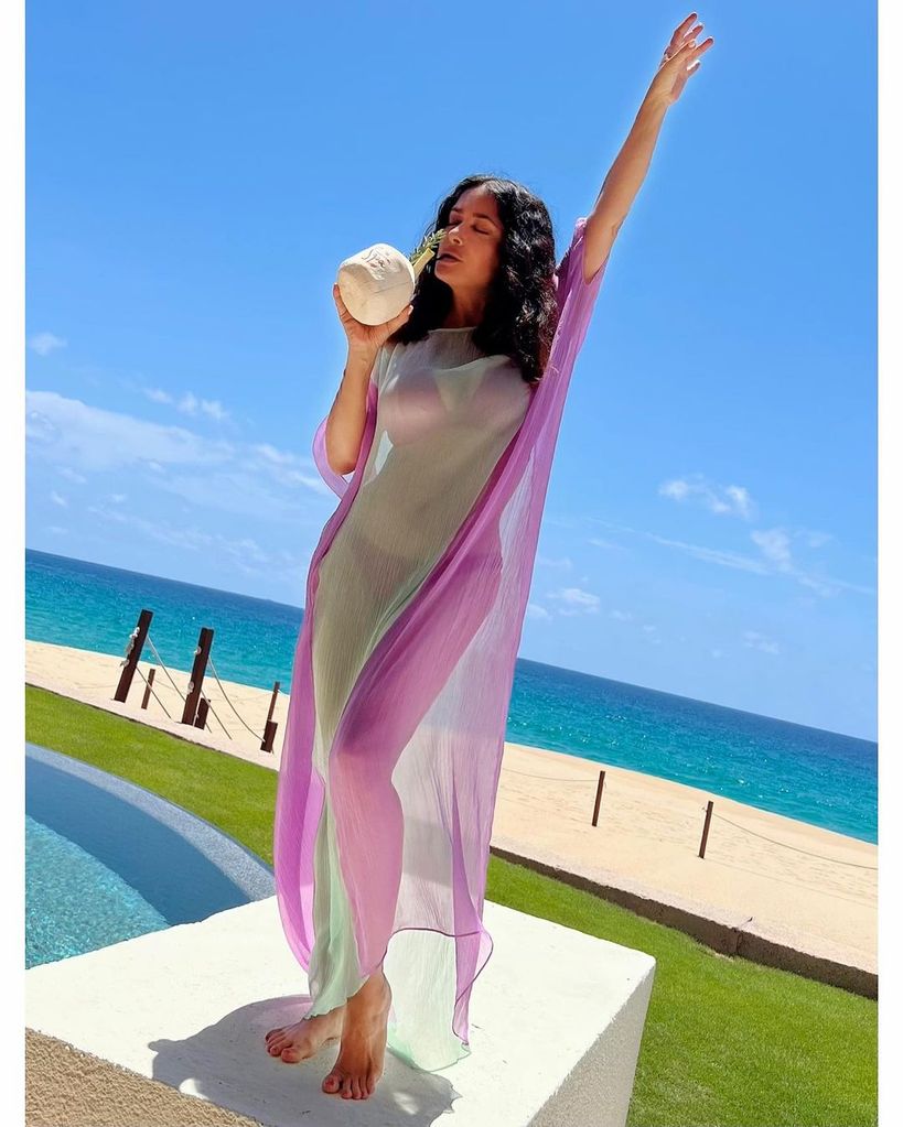 Salma Hayek wearing bikini and sheer cover up drinking cocktail by beach