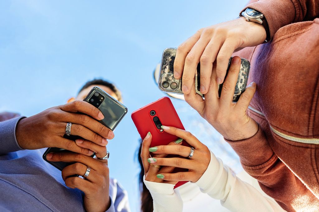 Low angle view of three young people using mobile phones outdoors.