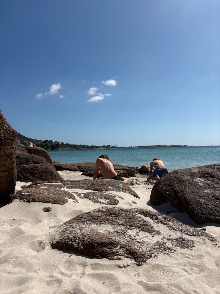 Two boys on the beach playing whilst sitting in the sand