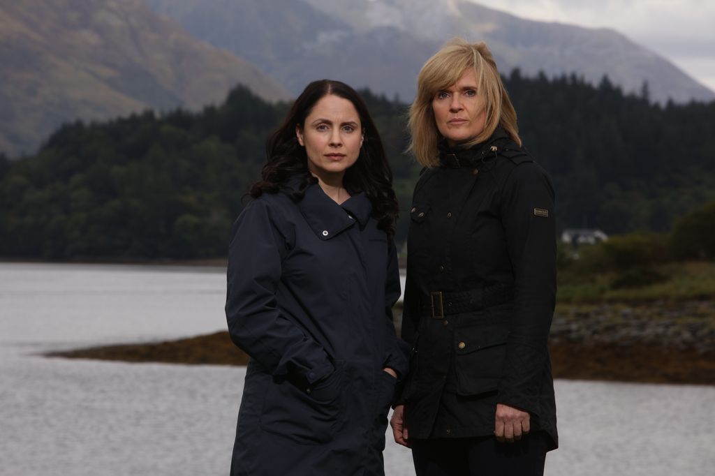 two women standing in front of lake and moutains