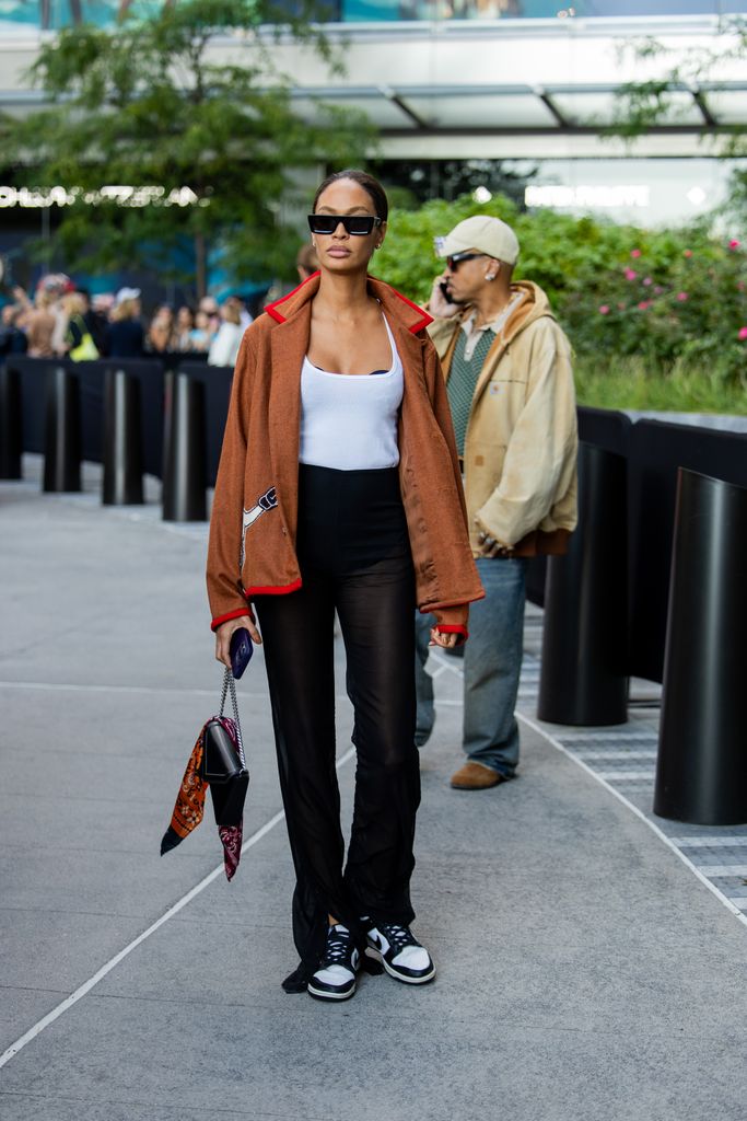 Joan Smalls wears brown jacket, black pants, white shirt outside Michael Kors during New York Fashion Week on September 10, 2024 in New York City