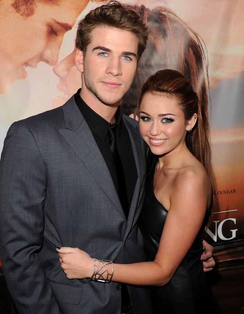 Liam Hemsworth with his arms around Miley smiling