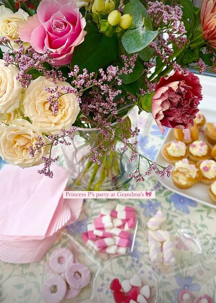 A selection of sweets by a pile of napkins, group of cupcakes and a vase of flowers