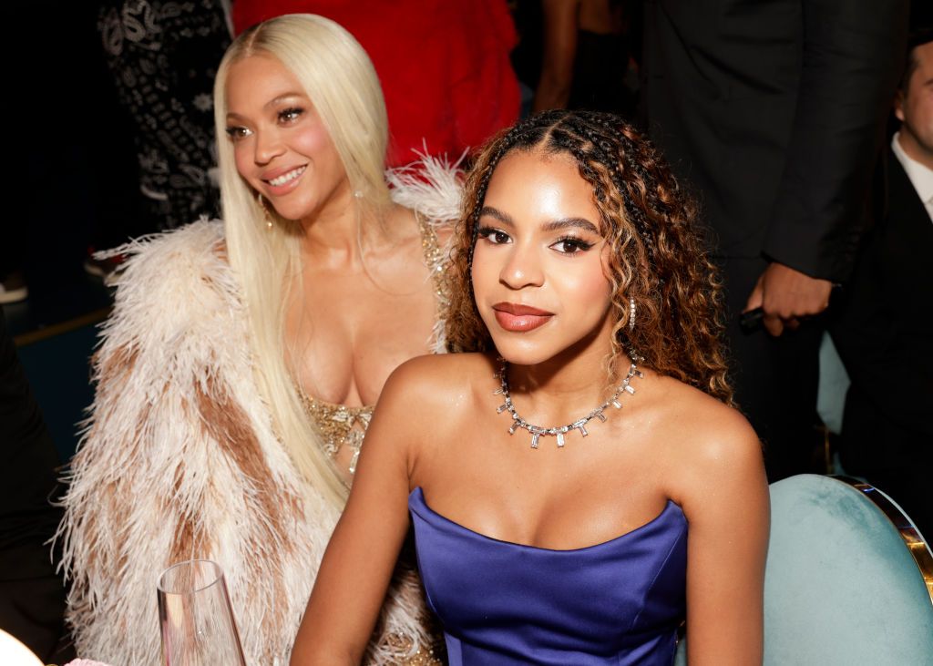 blue ivy sits in a blue dress with beyonce who is wearing white fuzzy coat