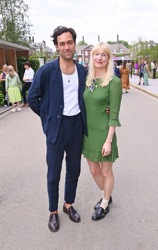 Alex Hassell in a navy suit and Emma King in a green mini dress with Mary Janes pose together at the Chelsea Flower Show 2025.