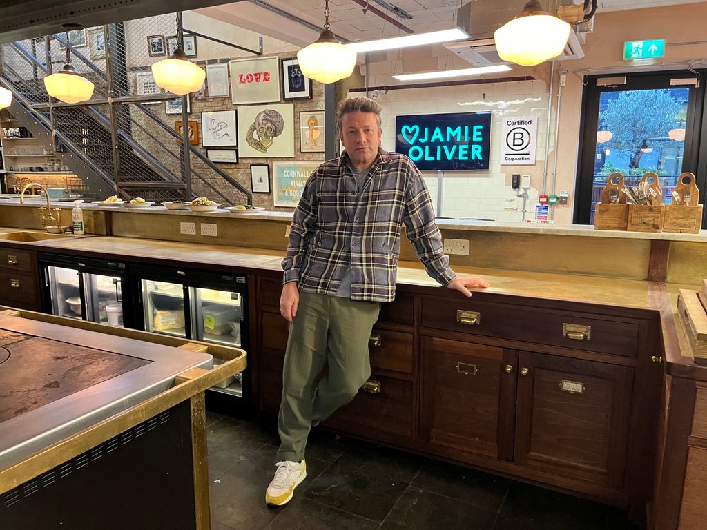 Jamie Oliver in a check shirt leaning on a kitchen counter top