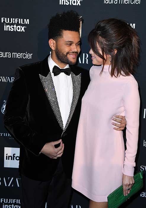 The Weeknd and Selena Gomez smiling at each other while posing on a red carpet
