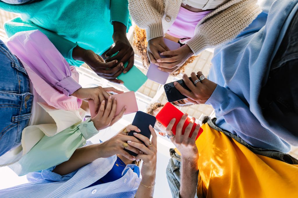 Low angle view of young group of people holding cellphone devices at city street. D