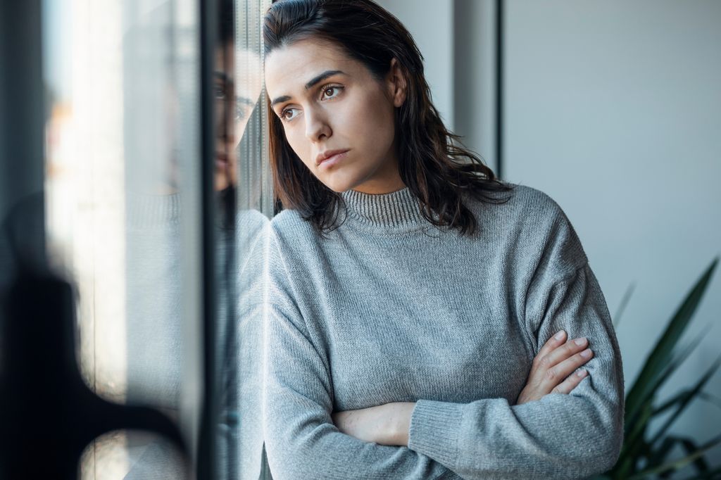 Woman staring out window in grey jumper