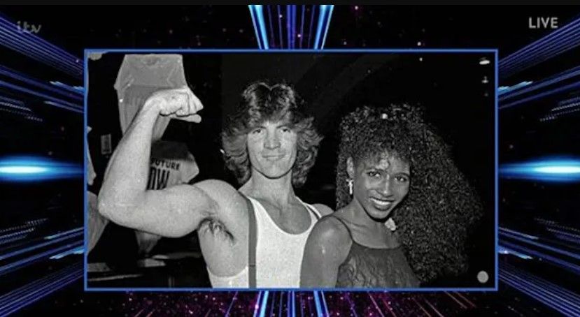 simon cowell with long hair and showing off muscles posing with sinitta in throwback photo 