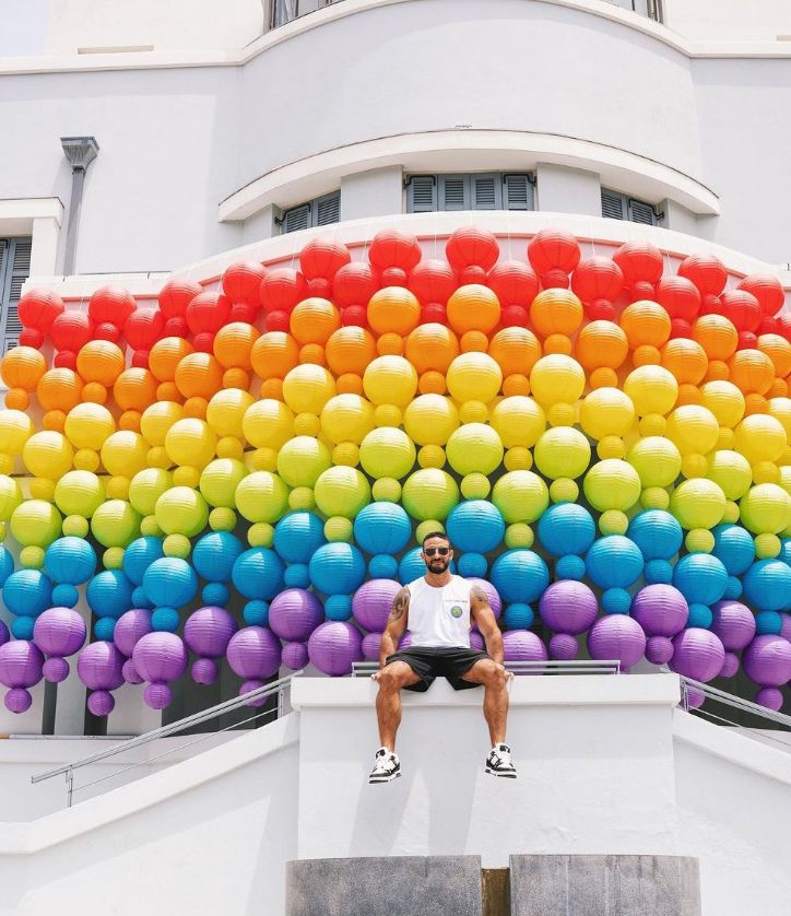 Eliad Cohen sat in front of a series of balloons in rainbow colours