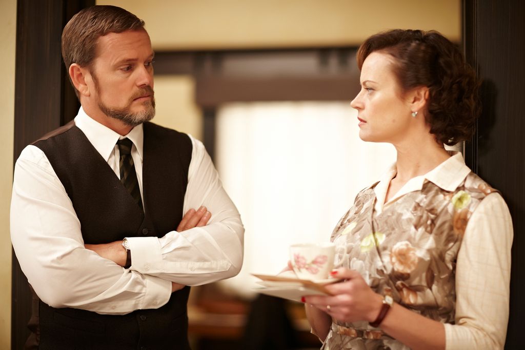 man in suit next to woman holding tea cup