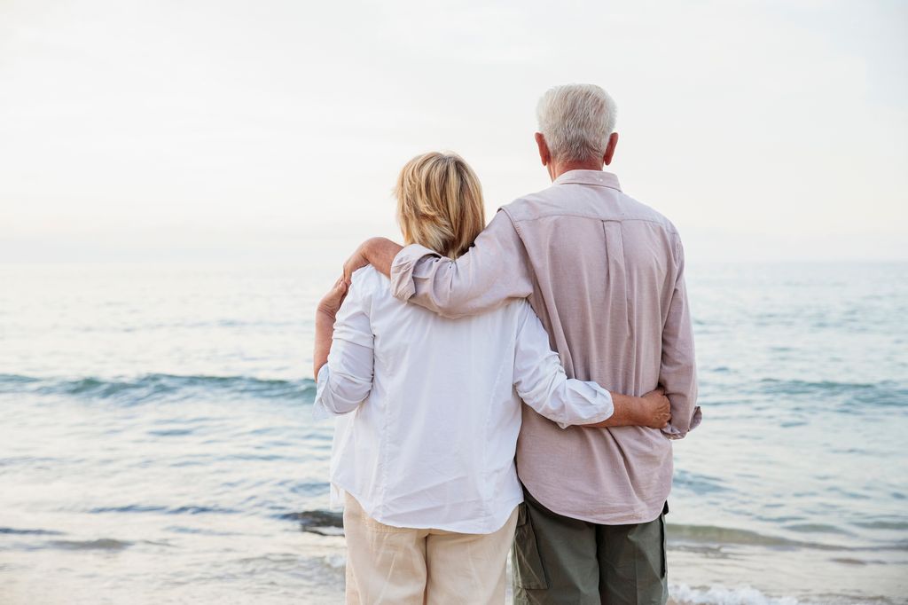 retired couple hugging on the beach seen from behind