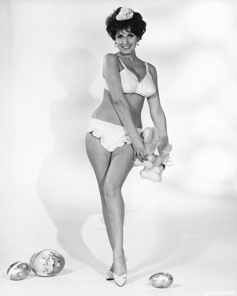 Yvonne Romain in a white bikini holds a plush bunny and poses with decorative eggs.