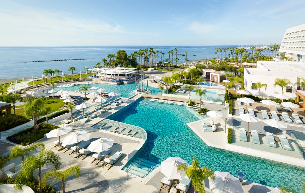 two large swimming pools with surrounding sun loungers and palm trees