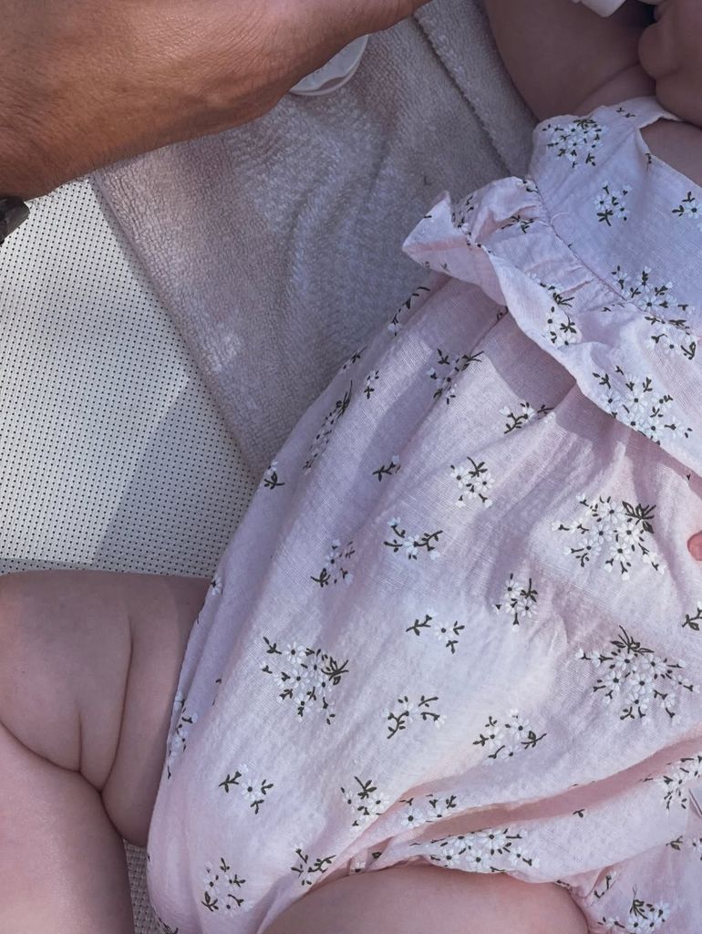 Photo of baby Palma lying down in a pink romper with her face cropped out of the frame