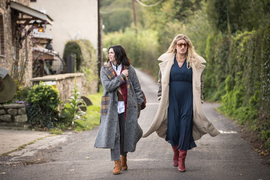 Two women wearing coats walking down a country lane