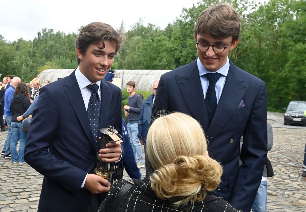 Prince Aymeric of Belgium and Prince Nicolas of Belgium in suits talking to woman