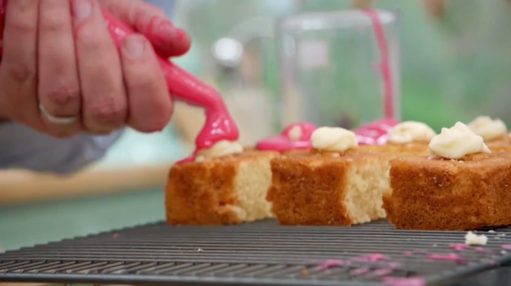 close-up of someone icing cake with pink icing 