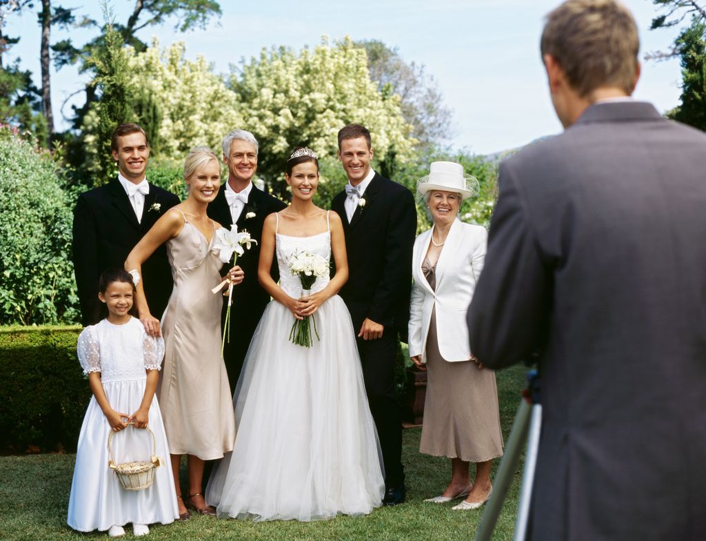 newlywed couple standing with their parents and guests and posing in front of a camera
