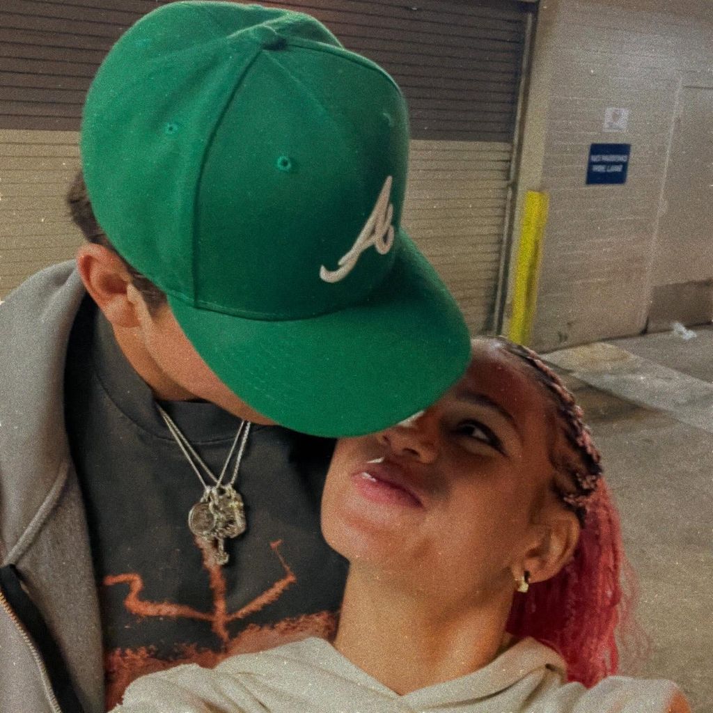 ben shelton wearing baseball cap while trinity rodman stares at hime