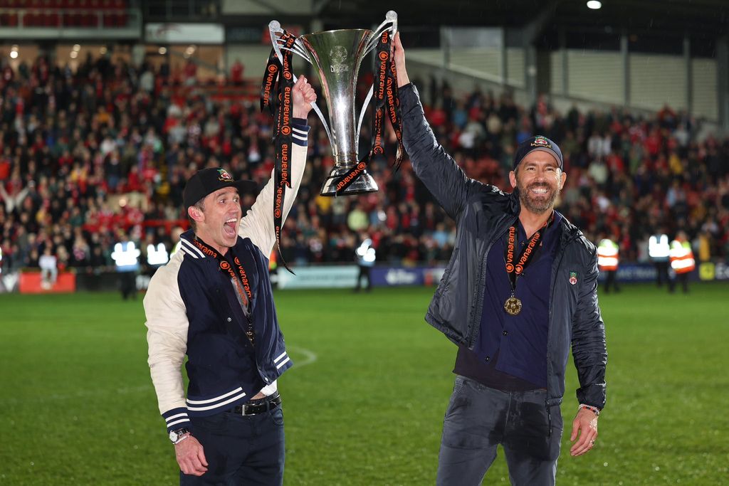 Ryan Reynolds and Rob McElhenney holding the National League trophy and smiling wide