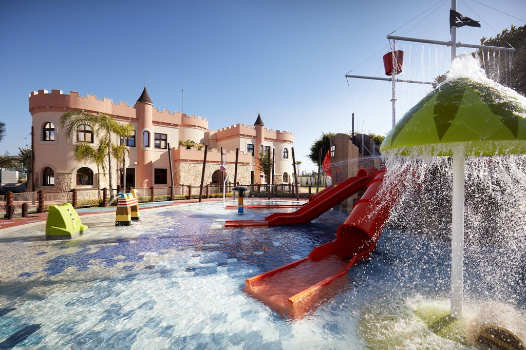 Outdoor activity pool with red slides connected to a pirate ship with castle in the background