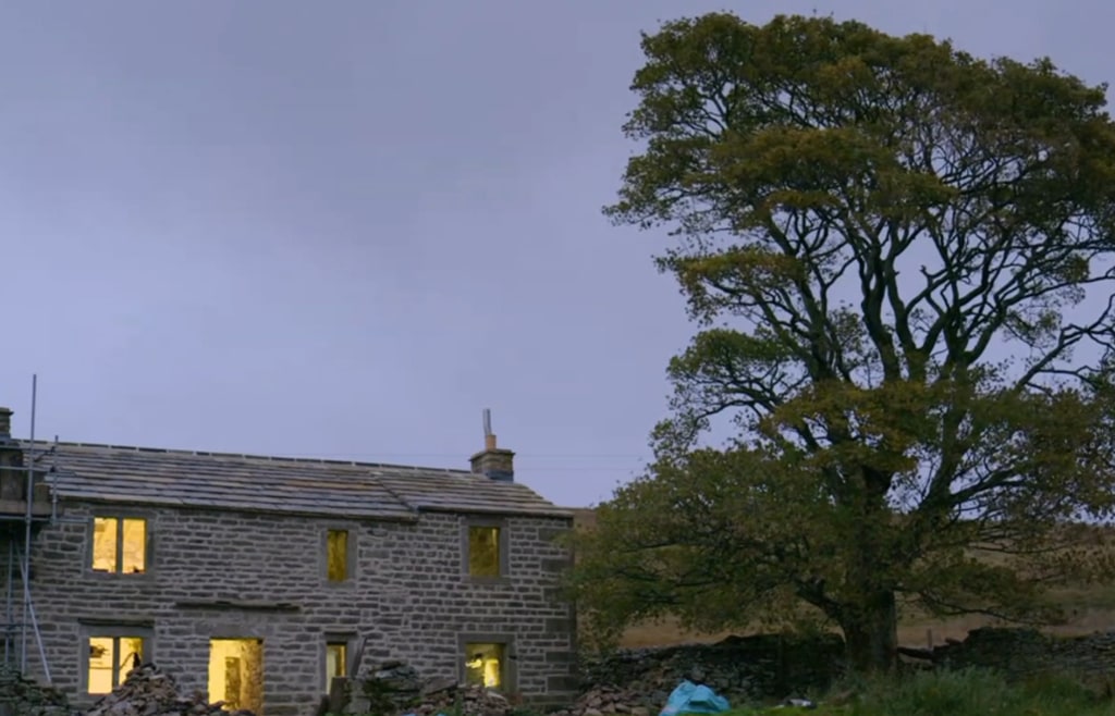 cottage with lights on next to large tree