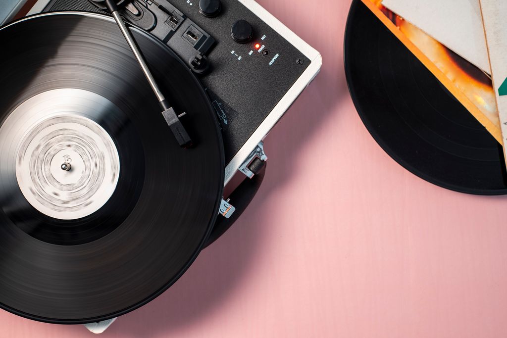 Turntable playing a vinyl record, surrounded by other vinyl records placed on the table. Photo taken from above for a dynamic, top-down view.