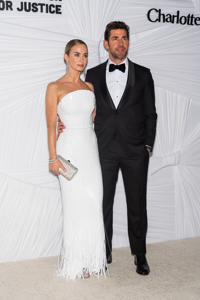  Emily Blunt in a white dress with her arm around John Krasinski in a suit and bow tie