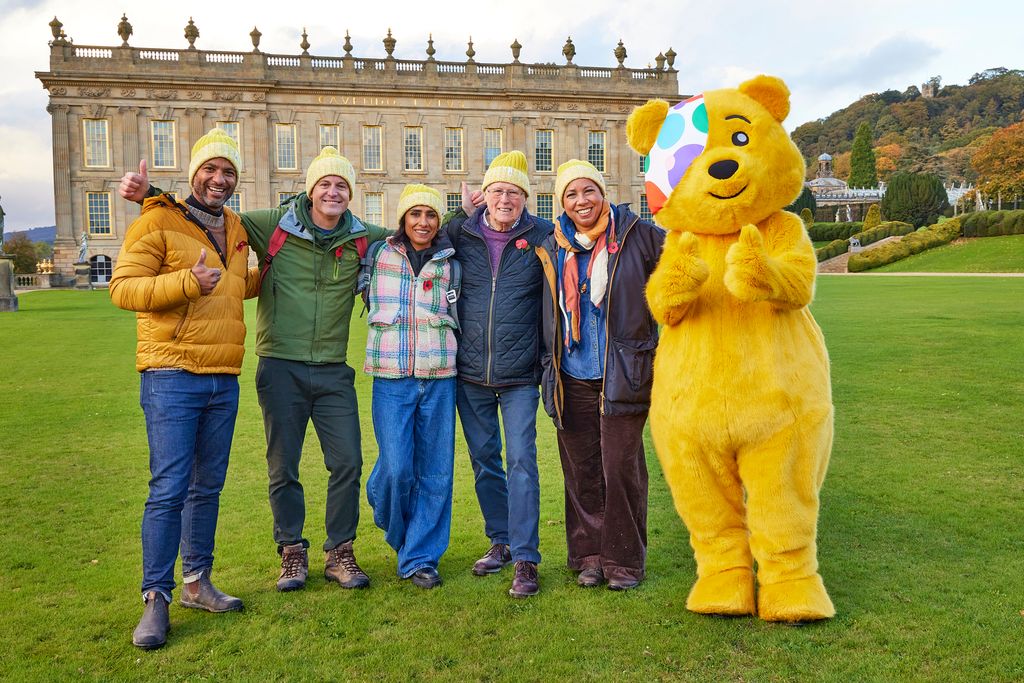 Five people and a yellow bear pose outside a big house on grass