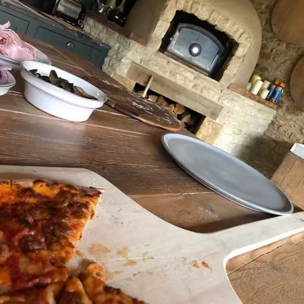 a lopsided photo of a partially eaten pizza on a table with a pizza oven a few meters away