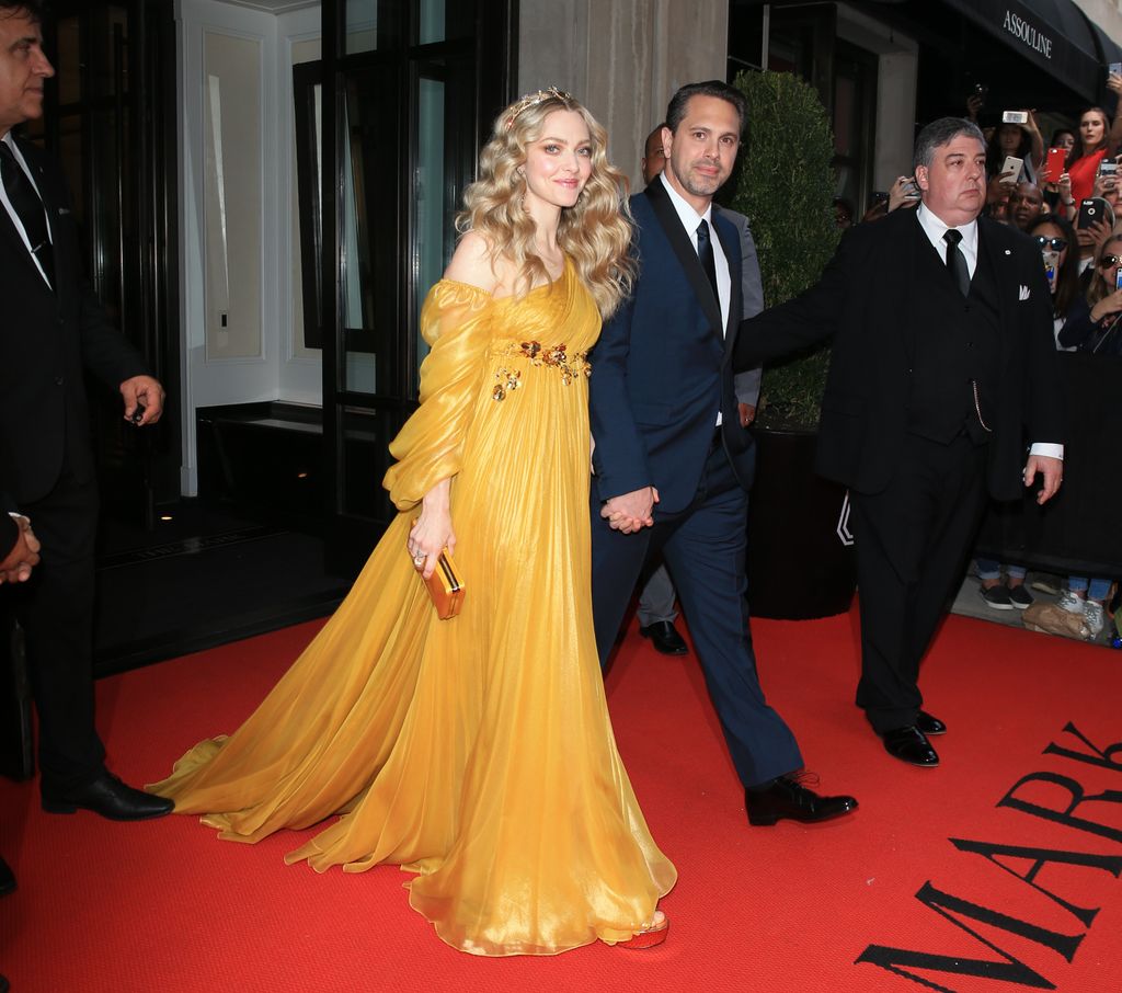 Amanda Seyfried in a mustard yellow dress holding hands with Thomas Sadoski
