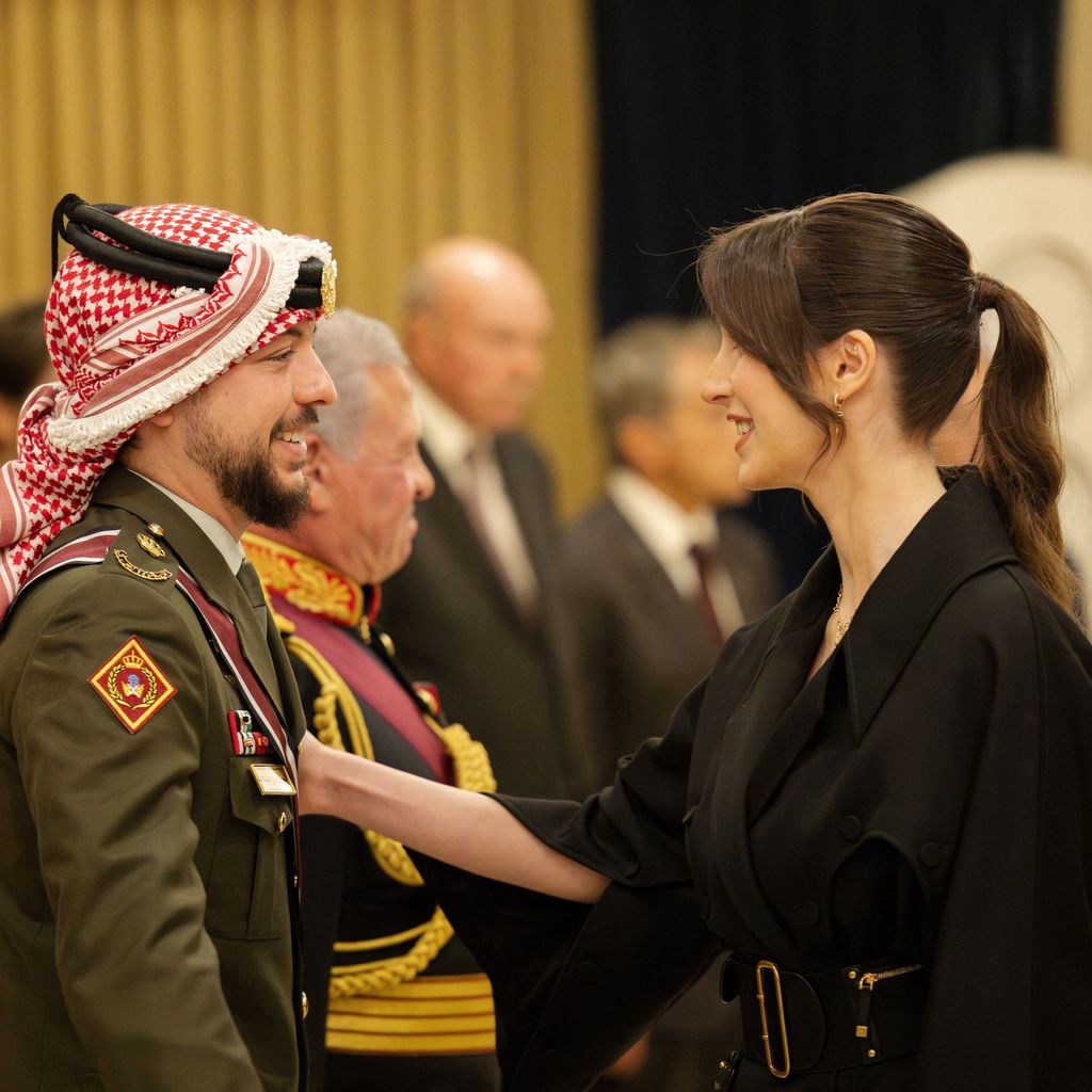 Crown Prince Hussein in military uniform and his wife Princess Rajwa in black smiling at eachother