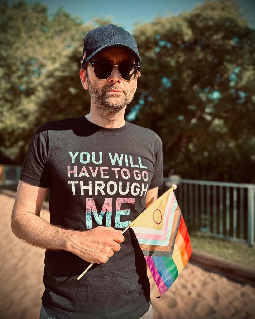 David Tennant wearing transgender rights T-shirt while holding Progress Pride flag 