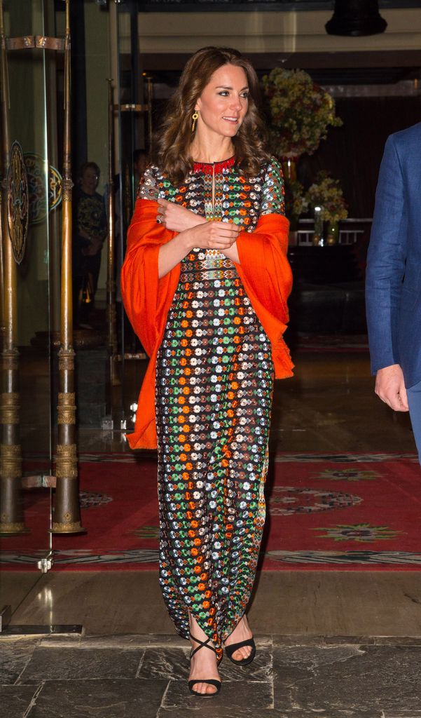 Kate in printed dress and orange shawl exiting hotel at night
