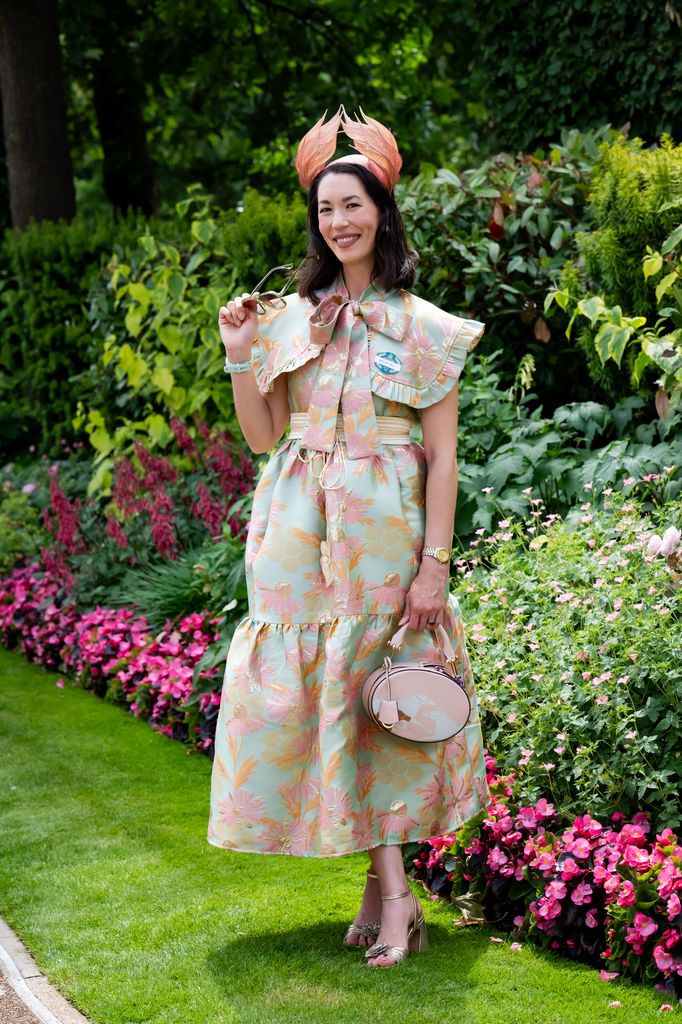 Lisa Tan attends the 1st day of Royal Ascot wears a mint and peach floral dress with an oversized collar, orange feathered fascinator, and circular pink handbag. (wearing a Lisa Tan hat and Sister Jane dress)