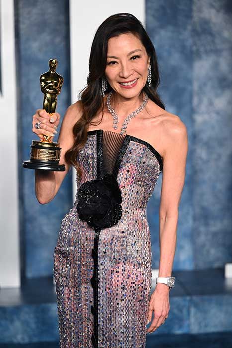 Michelle Yeoh smiling and holding up her Oscar award