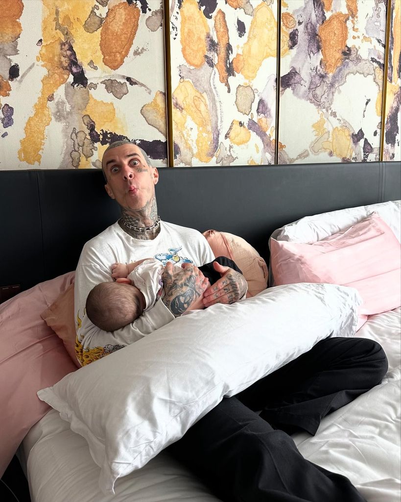 Travis Barker sitting in bed holding baby Rocky 