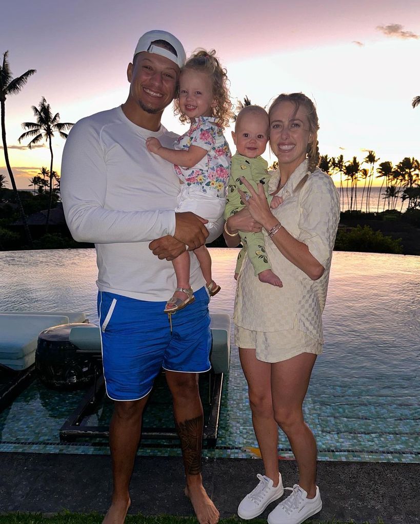 Patrick and Brittany Mahomes hold their children in their arms as they pose for pictures in front of palm trees and the ocean