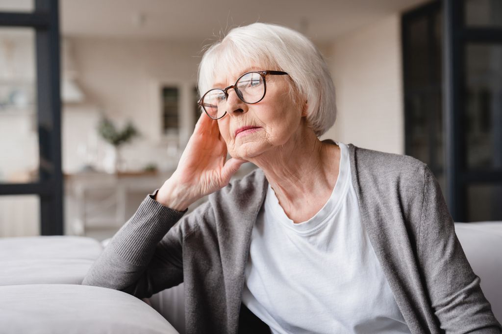Elderly woman in a T-shirt with her head resting on her hand looking into the distance