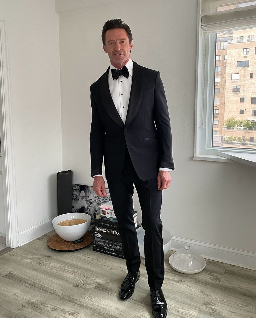 Hugh Jackman in a suit and bow tie near a window