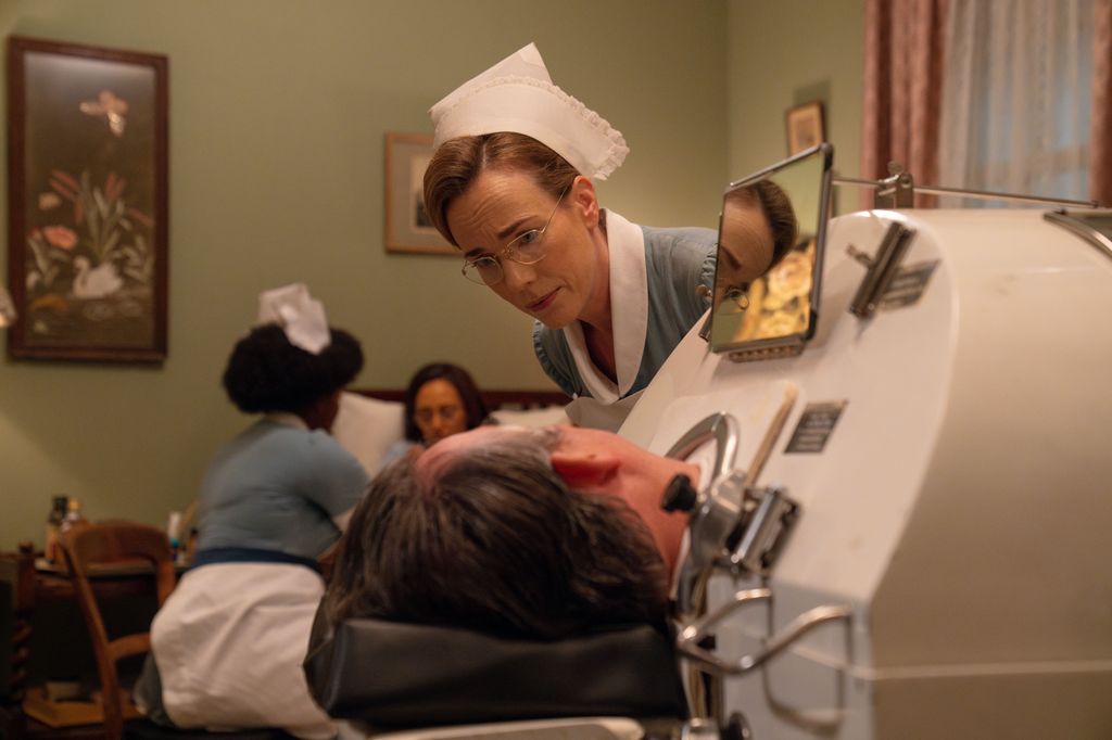 Woman in nurse uniform looking down at man in metal chamber