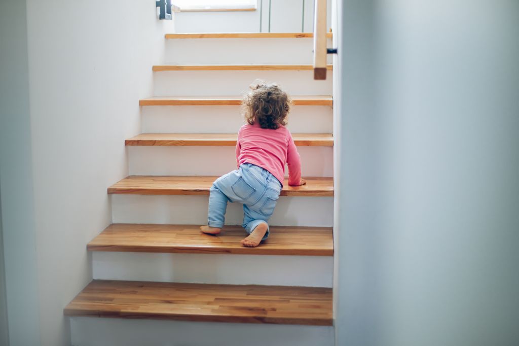 toddler girl climbing on stairs at home